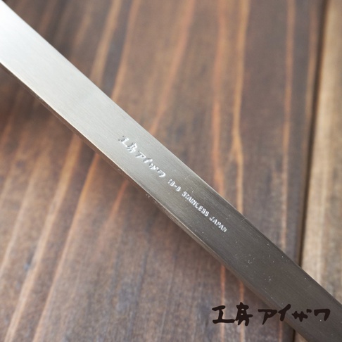 不鏽鋼萬用撈泡勺，銀色，表面刻有「工房アイザワ 18-8 STAINLESS JAPAN」字樣，置於木紋背景上。