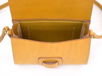 職人手作皮革寬扣帶馬鞍包，焦糖色牛皮材質，包身線條簡潔，頂部翻蓋開啟，內部空間寬敞，細緻的車縫線展現手工質感，搭配金色金屬環扣。