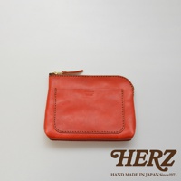 橘紅色皮革小物收納包，正面有一個貼袋，配有金色拉鍊，邊緣以深色縫線勾勒，展現皮革紋理。