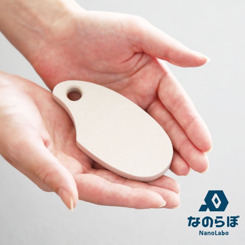 一塊米白色、橢圓形、帶有掛孔的珪藻土防潮塊，置於兩隻展開的手掌中。