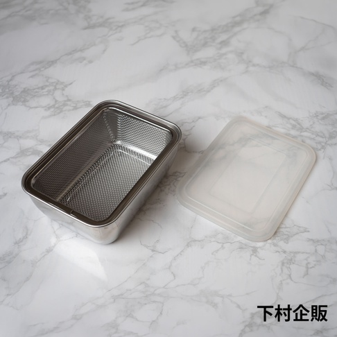 一個放置在大理石紋路桌面上的下村企販不鏽鋼長方形調理保存盒，容器內部配有可拆卸的金屬濾網，旁邊放著一個半透明的塑膠蓋，整體呈現簡約實用的廚房收納風格。