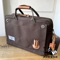 深棕色純綿帆布商務公事包，B4尺寸，配有皮革提把與肩帶，正面有鈕扣裝飾及品牌標籤，簡約實用。