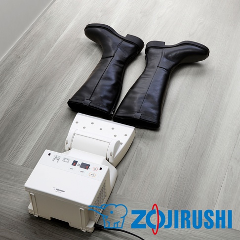 一組黑色皮質長靴，置於白色多功能智慧烘乾機上，烘乾機為方形主機，帶有可折疊的烘乾管，面板上有數字顯示和按鈕。