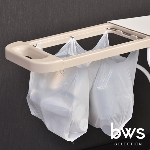 bws SELECTION 簡約滑蓋式分類垃圾架，米白色塑料支架，掛著兩個透明塑膠垃圾袋，其中一個垃圾袋內有白色物品，背景為深灰色紋理牆面。