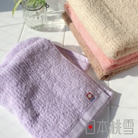 一條紫色細絨毛巾，搭配一疊米色、粉紅色和淺棕色毛巾，皆為柔軟材質，帶有細緻紋理，角落有品牌標誌。