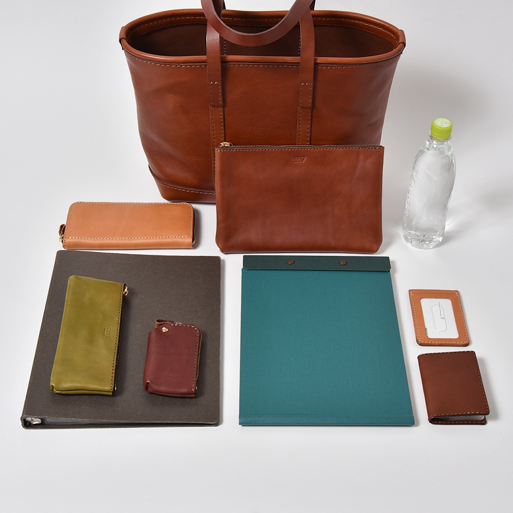 職人手作皮革經典托特包 T-9 M，搭配同色系皮革長夾、零錢包、收納包、筆記本及卡夾，另有一瓶透明水瓶。