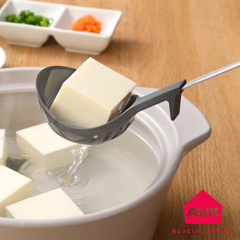 AUX 品牌紅房子標誌下方有日文小字，圖片顯示一個灰色濾水湯匙從裝有方塊豆腐和水的鍋中撈起一塊豆腐。