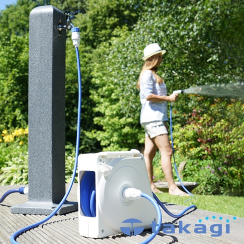 白色捲線器連接藍色水管，水管一端連接至灰色水龍頭柱，另一端由身穿條紋上衣與短褲、頭戴草帽的女性持握灑水槍澆灌花園。