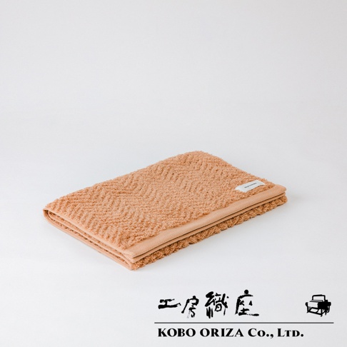 ECOR 天然系人字紋有機棉毛巾，採柔軟的淺棕色調，表面織有獨特的人字紋理，觸感蓬鬆，邊緣帶有精緻的縫線。