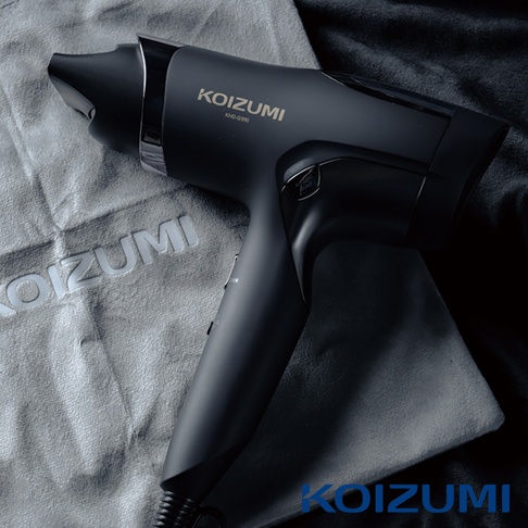 一隻黑色的KOIZUMI吹風機放在灰色和黑色的布料上，吹風機上印有KOIZUMI和KHD-G390的字樣