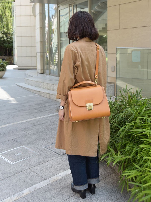 棕色皮革手提包，帶有可拆卸肩帶，包蓋上有金色鎖扣，皮革縫線清晰可見。