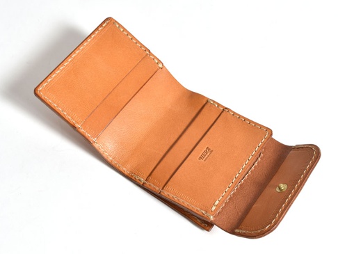 職人手作皮革方形短夾，採用鞣製皮革製作，呈現自然的棕褐色調。錢夾內部有卡槽和一個銅扣零錢袋，以白色縫線加固邊緣，展現精緻工藝。
