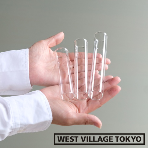 雙手捧著三個透明玻璃管，玻璃管材質光滑，呈現不同長度，背景為淺灰色。