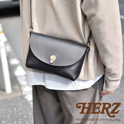 黑色皮革迷你單肩手袋，配有金色金屬旋轉鎖扣，斜挎在身著米色毛衣的模特身上。