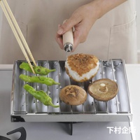 瓦斯爐專用炭烤風萬用燒烤盤，不鏽鋼材質，烤架上擺放著綠色的辣椒、香菇和烤飯糰，旁邊有雙筷子夾著辣椒。