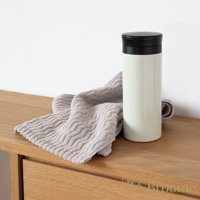 Broome 品牌下的 ASH 今治柔韻波紋甘撚細毛巾，以淡奶油色保溫瓶和灰色毛巾擺放在木質桌面。
