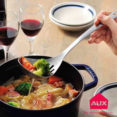 一支銀色金屬濾湯火鍋杓，杓面有孔洞，盛有花椰菜、紅蘿蔔和培根塊，正從一鍋熱騰騰的火鍋中撈起食材。