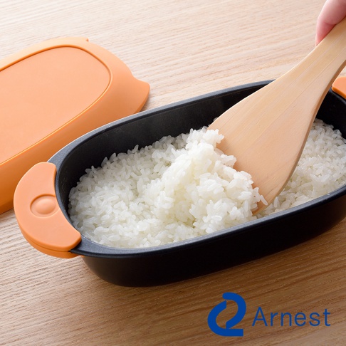 Arnest 標誌旁，木製飯勺正從裝滿米飯的黑色便當盒中盛起米飯，橘色的蓋子放在一旁。