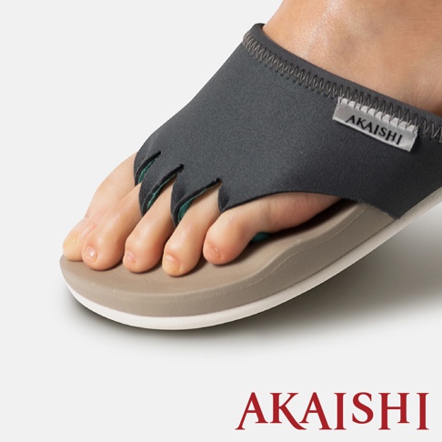 灰色五指訓練拖鞋，鞋面為彈性材質，內側飾有綠色滾邊，鞋底為雙層設計，外層淺棕色，內層白色，標有「AKAISHI」字樣。