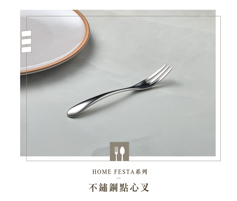 一個銀色不鏽鋼點心叉，放在淺灰色紋理桌面上，旁邊有一個部分入鏡的白色盤子，盤子邊緣有金色裝飾。