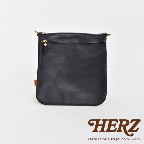 黑色皮革製成的直式斜背包，正面設有拉鍊開口，搭配金色拉鍊頭。包包側面可見棕色皮革拼接，並掛有品牌標籤。