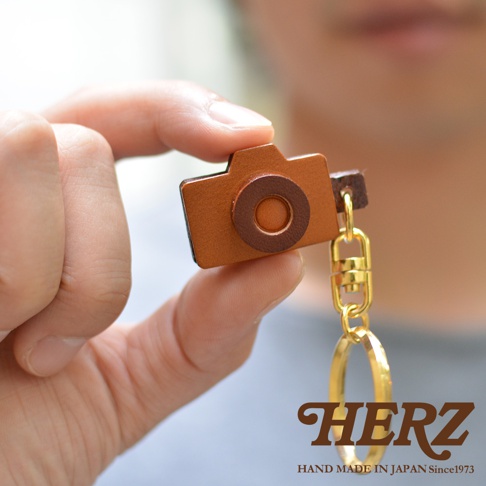 職人手作皮革相機造型鑰匙圈，以棕色皮革製成，造型小巧可愛，搭配金色金屬掛環及鑰匙圈。