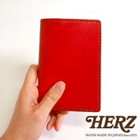 一只手持著紅色皮革護照套，邊緣有縫線裝飾。