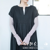 女性身穿深灰色洋裝，內搭一件淺粉色、帶有網狀編織紋路的有機棉長袖袖套，袖套從手腕延伸至手肘，袖口有流蘇裝飾。