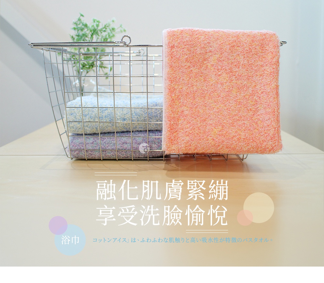 一個銀色金屬網架籃子放置在淺色木紋桌面上，籃內層疊著藍色與紫色的蓬鬆毛巾，籃外則懸掛著一條醒目的粉橘色毛巾。圖片下方以繁體中文與日文標示著關於洗臉愉悅與浴巾觸感的文字內容。