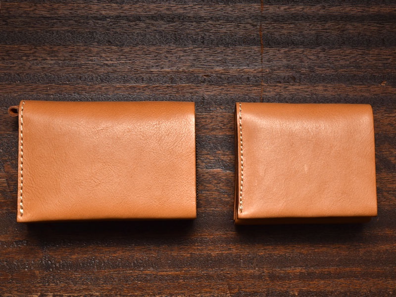 兩個棕褐色皮革短夾，皆為直式卡片收納雙折設計，左側款有掛繩，兩款皆有明顯的縫線。