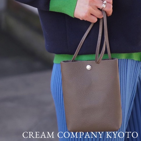 咖啡色皮革隨身手機包，有細緻的紋路和縫線，上方有銀色按扣，搭配短提把。