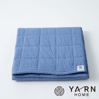 一條藍色、以格紋縫製的浴巾，由脫脂棉混紗製成，質地柔軟，邊緣有品牌標誌。