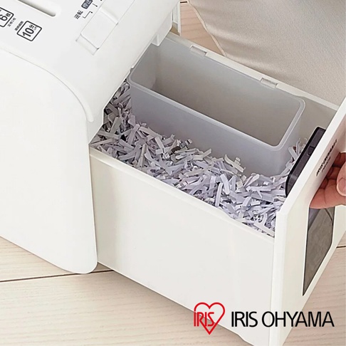 白色塑膠碎紙機，內部有透明塑膠碎紙收集盒，裝滿了細小的紙條。碎紙機上方有按鈕和標示。