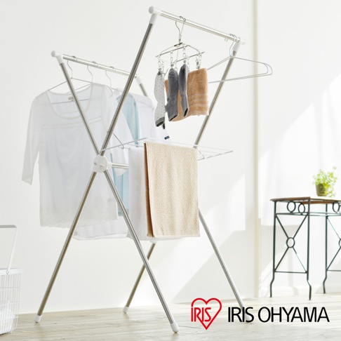 一個不鏽鋼材質的X型曬衣架，架上掛有白色上衣、淺藍色衣物、兩條毛巾，上方還有一個掛滿襪子的小型曬衣夾。