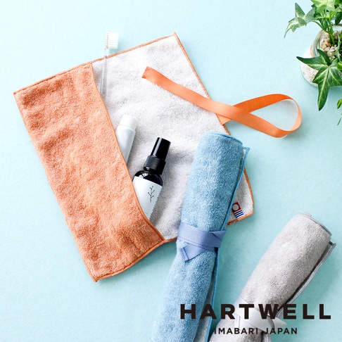 今治速乾毛巾收納袋，橘色毛巾內含牙刷、牙膏和噴瓶，另有藍色與灰色兩款捲起並以同色系緞帶綁住的毛巾。