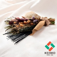 乾燥花束，包含紫色、粉色、米色、綠色等乾燥植物，搭配麻布裝飾，束綁於一側，底部為黑色細長條狀物。