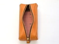 咖啡色皮革圓角收納筆袋，拉鍊開啟，內有紅色紙張，白色縫線裝飾。