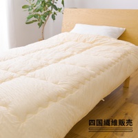 淺米色舒芙蕾四季被，採用細緻的縫線與蓬鬆的填充物，營造出柔軟的質感，覆蓋在木質床架上，一旁擺放著綠色植物。