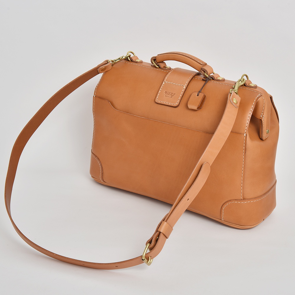 職人手作皮革公事包，呈現自然棕色，設有可拆卸肩帶和頂部提把，皮革材質散發質感，適合商務旅行。