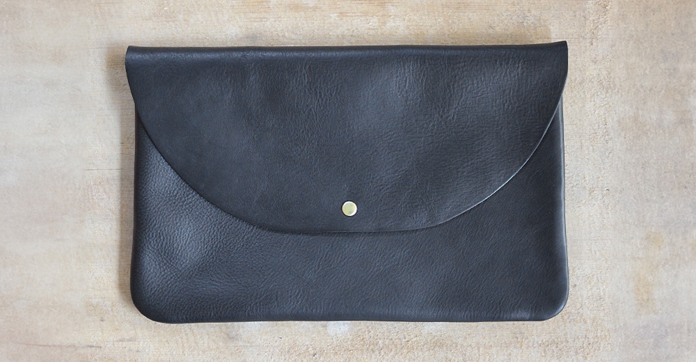 黑色皮革製成、帶有鈕扣式翻蓋的方形小物收納袋，材質為柔軟的皮革。