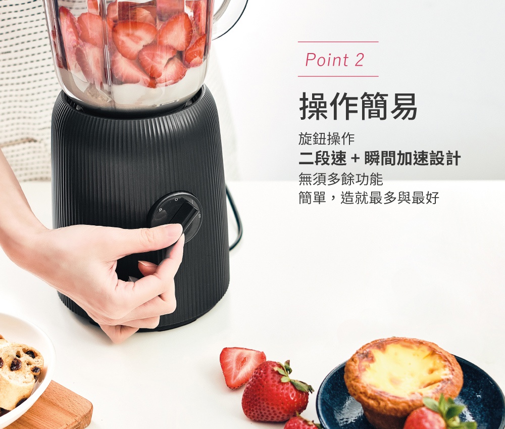 黑色條紋紋理果汁機，裝有切片草莓，右手正在操作側邊旋鈕。