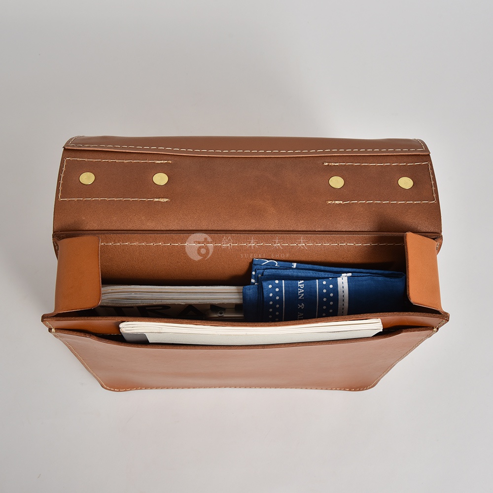 鞣製皮革製成的後背包，主色為棕色，內有雜誌和藍色印花布，包款設計簡約，有金屬釦飾及白色車縫線。