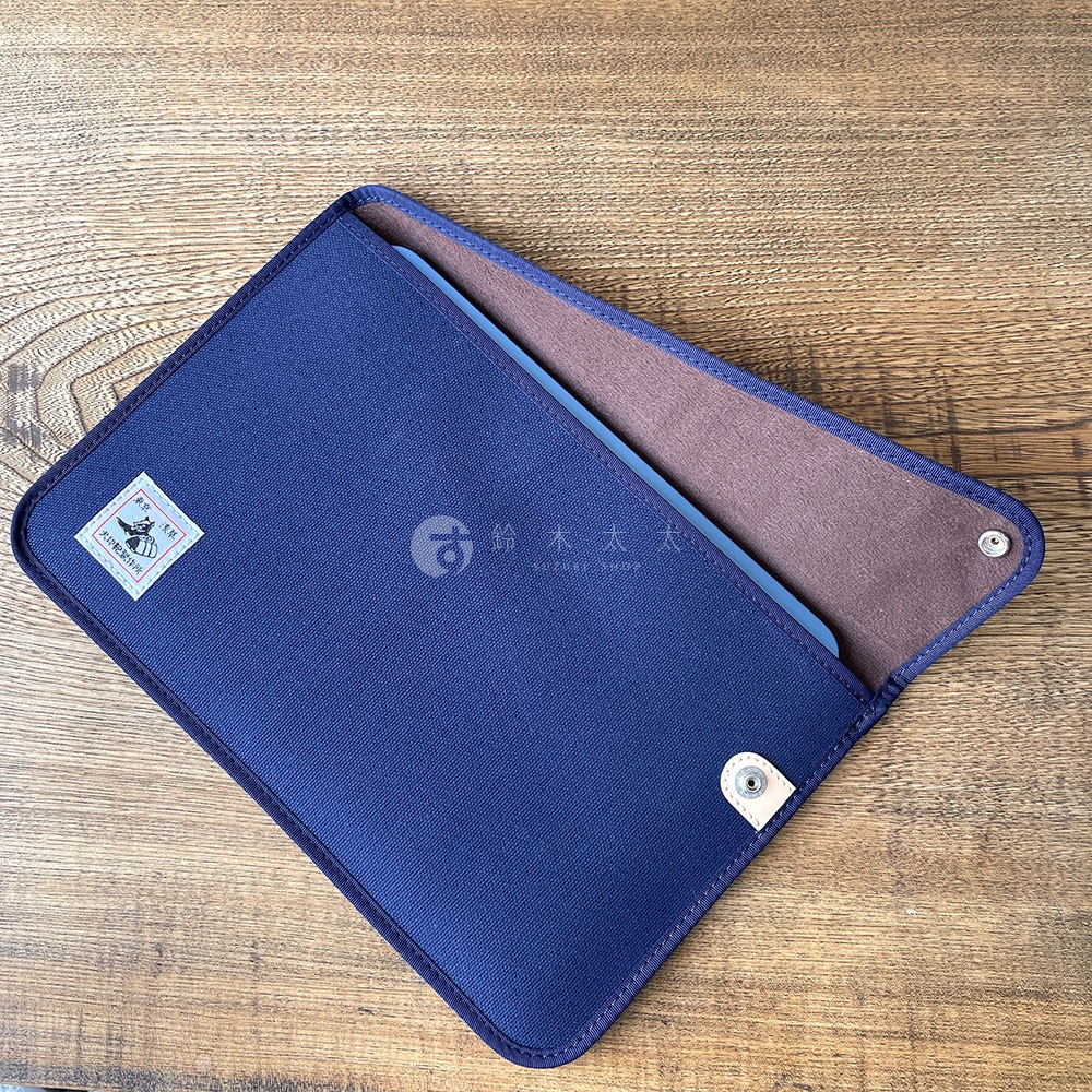 藍色純棉帆布平板收納包，內襯為棕色，有品牌標誌和金屬釦。