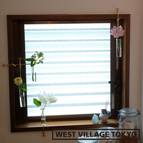 黃銅可夾式玻璃花器，懸掛於窗戶框架上，內插綠葉植物、白色玫瑰和粉色小花，玻璃試管狀，下方窗台上另有白色繡球花。