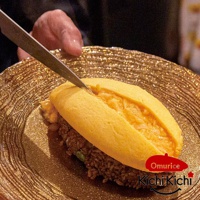 金黃色半熟歐姆蛋包裹著炒飯，用刀劃開。餐點盛放在帶有紋理的金色盤子上，盤子閃爍著光澤。