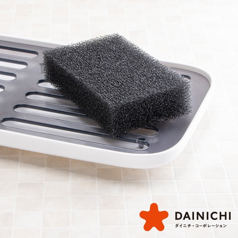 黑色海綿放置於白色帶有灰色網格的瀝水盤上，海綿表面有細密的氣孔。