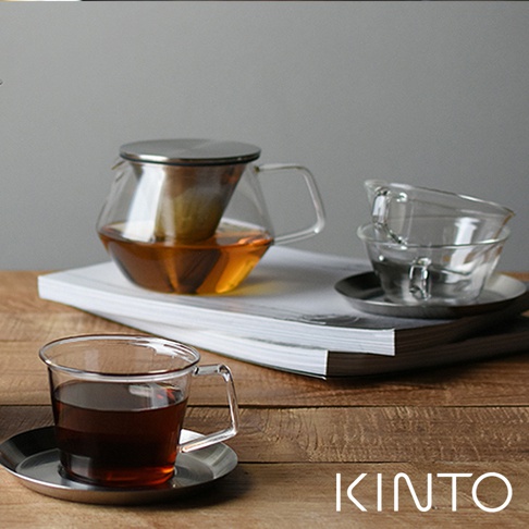 Carat 茶壺，容量 600ml，由透明玻璃製成，帶有金屬濾網和把手，壺內盛有琥珀色茶飲。旁邊還有兩個玻璃杯和一個茶杯，皆放在銀色茶碟上。