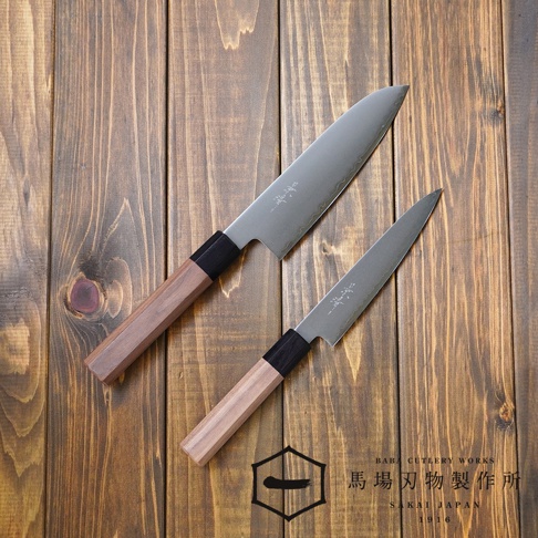 兩把景清 Chromax 鋼水果刀，刀刃為銀色金屬，手柄為胡桃木材質，搭配黑色連接處，置於深棕色木紋背景上。