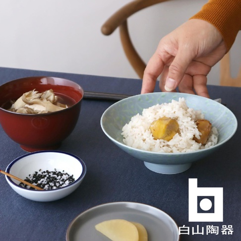 淺藍色花紋陶瓷飯碗盛有白米飯和兩塊栗子，旁邊是深紅色湯碗，內有香菇湯，以及裝有黑白芝麻鹽的小碟。
