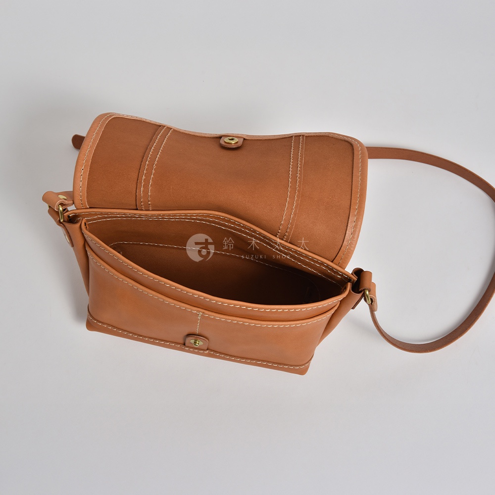 棕色皮革復古郵差包，翻蓋設計，有明顯的縫線細節，包身前方有兩個外袋，可見其皮革材質與金屬扣環。